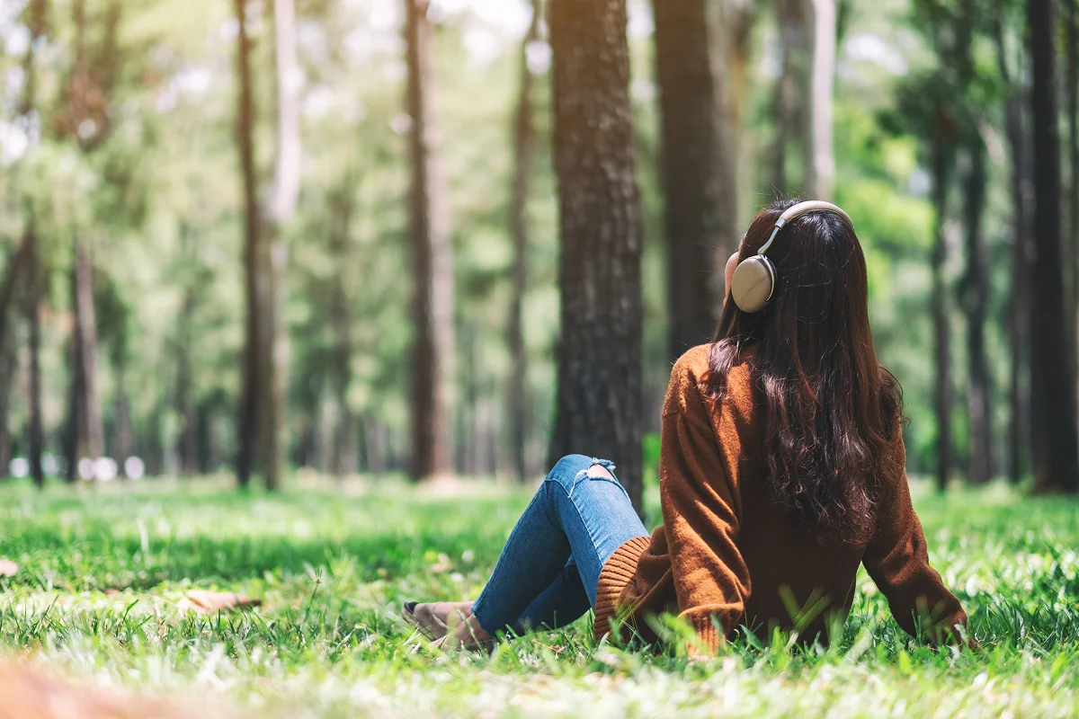 Person sitting down and listening to music on their headphones in the middle of the woods