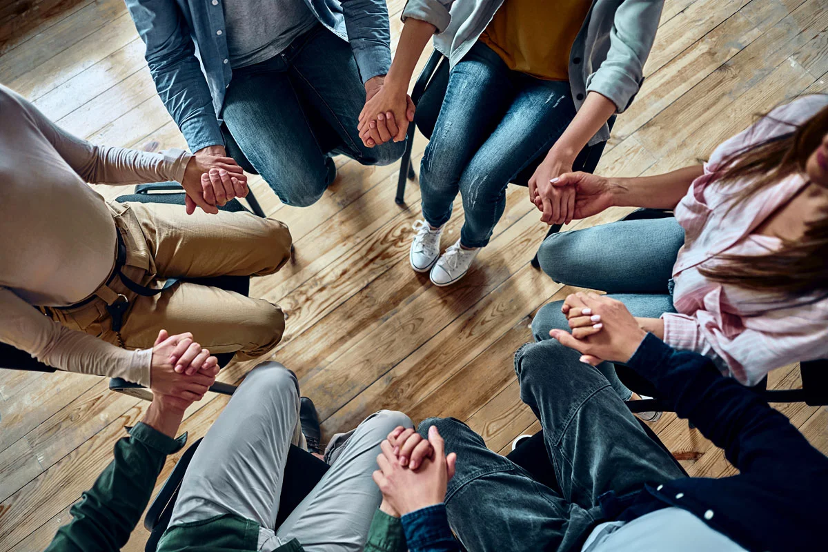 a group of people hold hands in therapy after cocaine detox