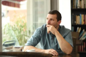 Man in blue polo sitting at a desk thinking about recovery treatment